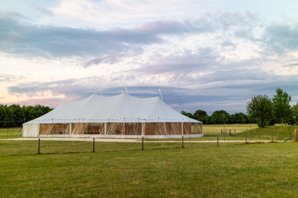 White outdoor event marquee tent set up in a large open field under a cloudy sky.