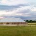 White outdoor event marquee tent set up in a large open field under a cloudy sky.